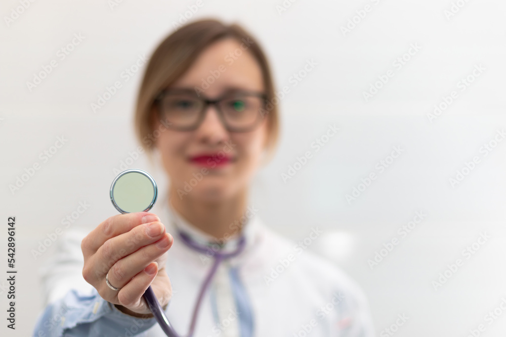 Beautiful young doctor woman in a medical coat and glasses with a stethoscope in a hospital on a white background. Selective focus. Portrait. Close-up Beautiful young doctor woman in a medical coat and glasses with a stethoscope in a hospital on a white background. Selective focus. Portrait. Close-up