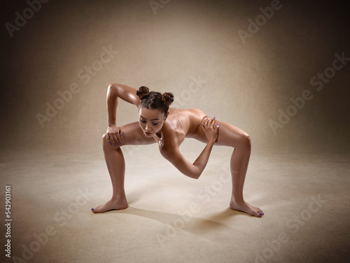 Beautiful nude sexy fitness girl with a great figure flexing her perfect body in a yoga pose at the studio. Spider pose.