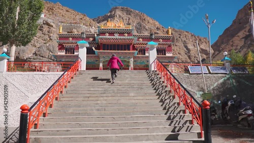 Slow motion Wide angle shot of young Indian girl tourist climbing stairs of Sakaya Tangyud monastery at Kaza, Spiti Valley, India. Budhhist monastery in background of Himalayan mountains. photo