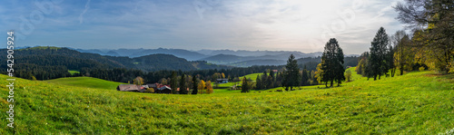 Herbstliches Panorama vom Pfänder über den Bregenzerwald, Dunst und Saharasand liegen in der Luft und schaffen ein mystisches Bild mit orangen und gelben Laubbäumen, Bauernhäuser und Dorf im Tal