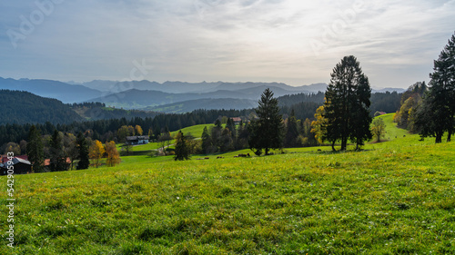 Herbstliches Panorama vom Pfänder über den Bregenzerwald, Dunst und Saharasand liegen in der Luft und schaffen ein mystisches Bild mit orangen und gelben Laubbäumen, Bauernhäuser und Dorf im Tal photo