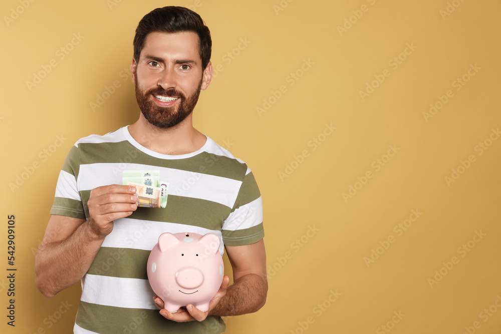 Happy man putting money into piggy bank on beige background, space for ...