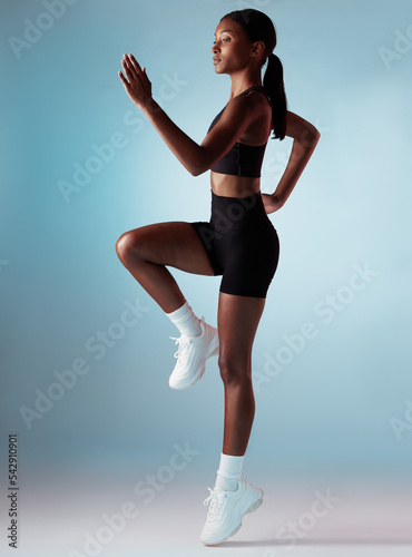 Sports, exercise and woman runner in studio with balance, form and motivation. Fitness, health and black woman from Jamaica running on blue background. Healthy girl cardio training for marathon race.