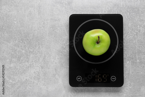 Digital kitchen scale with ripe green apple on grey table, top view. Space for text