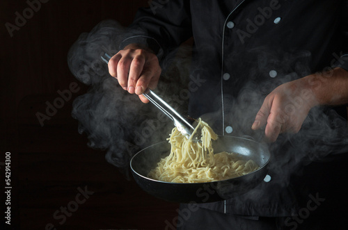 Cooking spaghetti in a frying pan in the hands of a chef. Space for advertising on a black background.