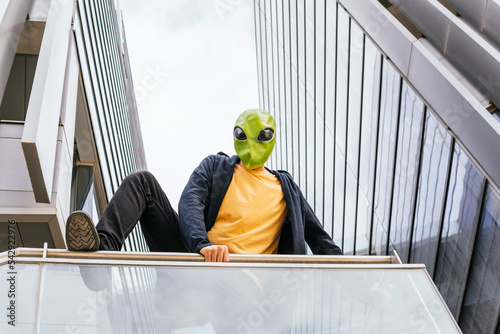Man wearing alien mask jumping over railing in front of building