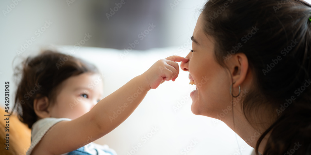 Cute little baby toddler playing and enjoying while in the arms of young mother hugging at home Cute little baby toddler playing and enjoying while in the arms of young mother hugging at home