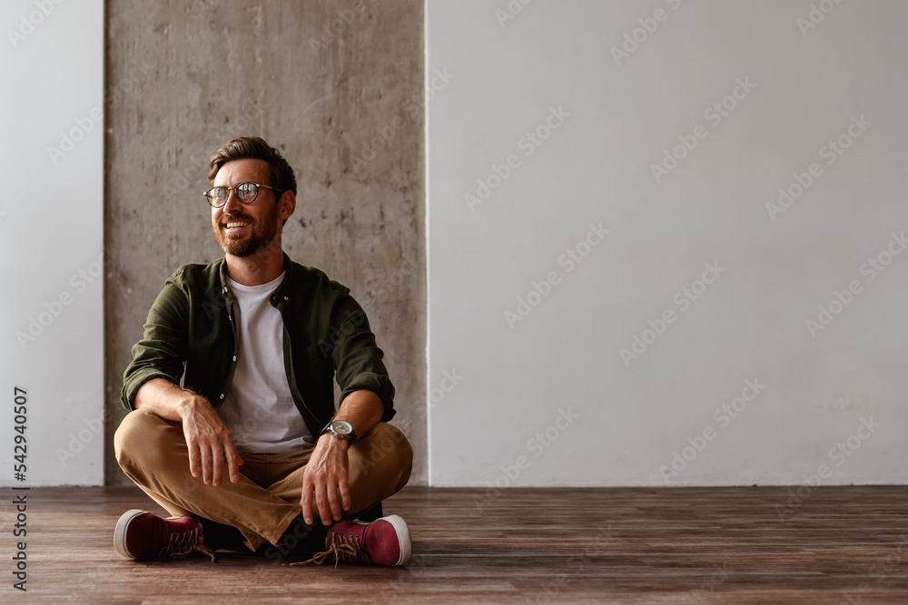 Fototapeta premium bearded interior designer smiling while sitting on floor in apartment 