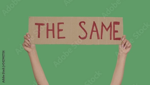 THE SAME. Protest text message on cardboard. Stop racism. Police violence. Banner design concept. Hands of women raising up poster on green screen, chroma key. Stop Racism concept, No Racism. photo