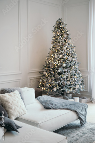 Christmas decor in a photo studio in gray and white. Snow-white Christmas tree, gifts and lanterns, sofa. out of focus. Place for a photo shoot.