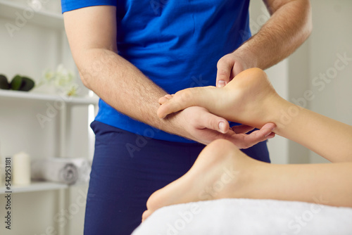 Professional reflexologist doing remedial therapeutic stress relieving foot massage to young girl. Specialist in acupressure and reflexology pressing special points and areas on female patient's feet