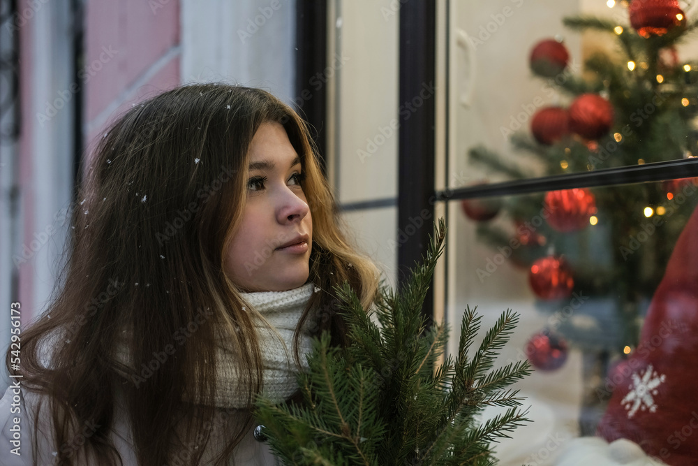 Young beautiful girl dreamily looking at shop windows decorated for Christmas Young beautiful girl dreamily looking at shop windows decorated for Christmas