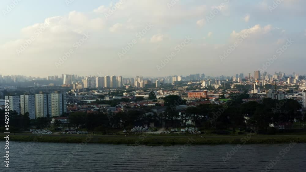 Aerial drone left trucking and panning shot of the south of São Paulo, Brazil from the man-made Guarapiranga Reservoir towards the Socorro neighborhood with skyscrapers and houses during sunset. Aerial drone left trucking and panning shot of the south of São Paulo, Brazil from the man-made Guarapiranga Reservoir towards the Socorro neighborhood with skyscrapers and houses during sunset.