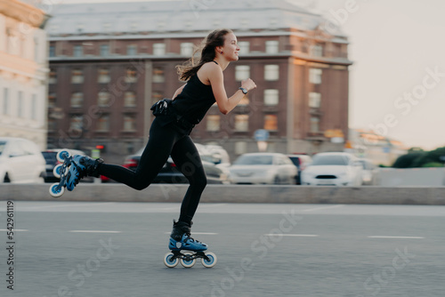 Athletic woman rides on rollers moves very fast dressed in active wear enjoys rollerblading being photographed in action poses at urban place engaged in extreme sport. Active lifestyle concept photo