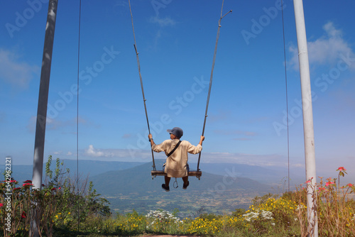 Asian tourists sitting alone on wooden swing and look at mountains like Fuji-san in Fuji in Thailand at Loei Province, Rear view while rest on Nature in summer seem so fun and happiness in lifestyle
