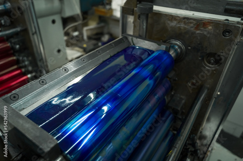 Cyan ink in the paint system compartment of a modern flexographic printing press in a print shop. Blue paint in the ink feeder on the printing cylinder. Selective focus