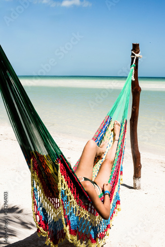 Woman in bikini lying in a hammock on the beach at the edge of the sea at Holbox, Mexico.