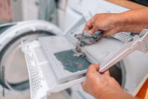 Dust and dirt trapped by the clothes dryer filter, female hand taking the lint out from dirty air filter of the dyer machine 