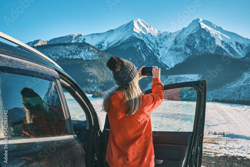 Woman traveling exploring, enjoying the view of the mountains, landscape, lifestyle concept winter vacation outdoors. Female standing near the car in sunny day