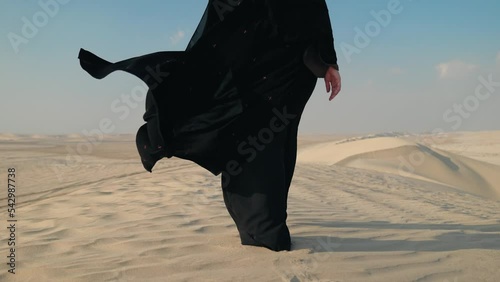 Close-up of girl in traditional Abaya dress walking barefoot along the dunes in the desert of Doha Qatar. 4K Slow Motion
 photo