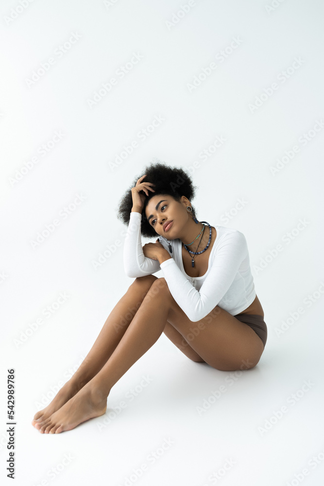 full length of dreamy african american woman in long sleeve shirt and panties sitting on white background.