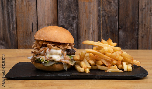 Monster burger. Multilayer hamburger with mozzarella cheese, meat, cucumber pickles, mayonnaise, lettuce and crispy onion, with french fries.