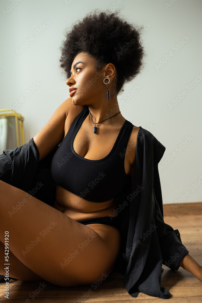 Side view of african american woman in black shirt and underwear sitting on floor in bathroom. Side view of african american woman in black shirt and underwear sitting on floor in bathroom.