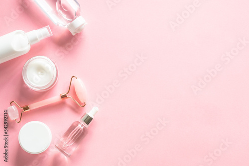 Natural cosmetics on pink. Skin care product, cream, soap serum, jade roller. Flat lay image with copy space.