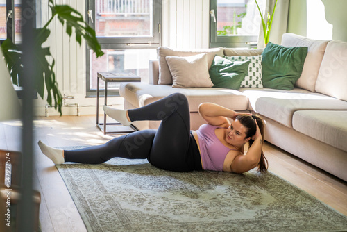 Full length view of the overweight woman training her abs alone at her apartments