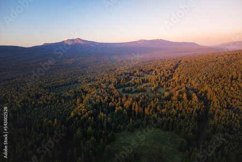 Aerial view of mountain range and forest beautifully lightened by the rising sun under clear morning sky