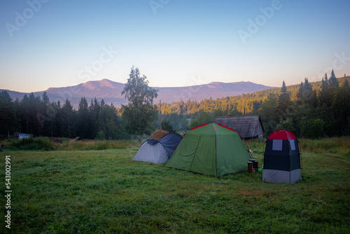 Tourist camp with tents in a clearing in a forest with a mountain range lightened by the rising sun in the background