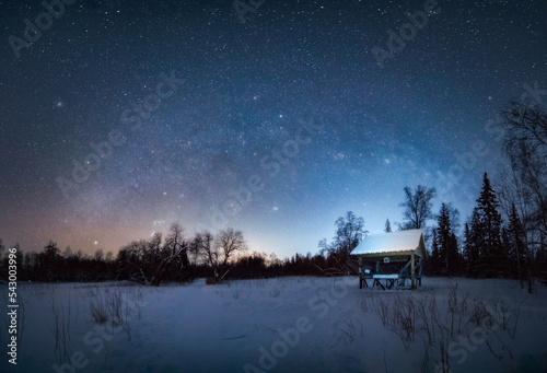 Mlky way Arc in the night sky above snow-covered garden house in winter forest