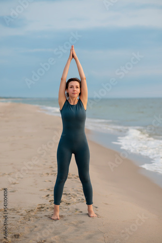 Woman in a blue sports jumpsuit does gymnastics on the seashore