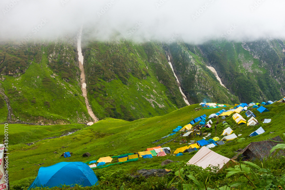 July 14th 2022, Himachal Pradesh India. Multiple colorful tents at Bheem Dwari base camp with beautiful mountains peaks and waterfalls in the background.