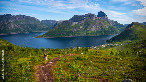 backpacker girl hiking hesten trailhead overlooking the town of fjordgard and mighty mountains in norway, senja island hiking, famous segla mountain photo