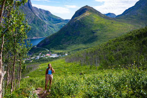 backpacker girl hiking hesten trailhead overlooking the town of fjordgard and mighty mountains in norway, senja island hiking, famous segla mountain photo