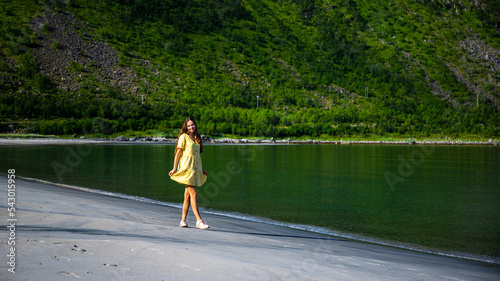 a beautiful girl in a yellow dress dances on a beach surrounded by mighty mountains on the island of senja in norway, holiday in the norwegian fjords, steinfjord photo