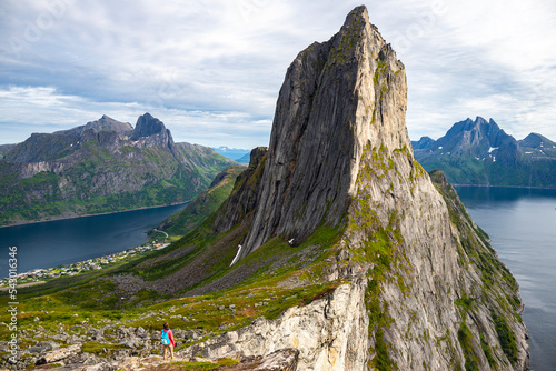 backpacker girl hiking on hesten overlooking Norway's famous segla mountain, senja island; hesten trail head, Norway's famous fjords with mighty mountains above the sea photo