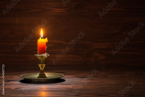 burning old candle with vintage brass candlestick on wooden background in minimalist room interior, copy space