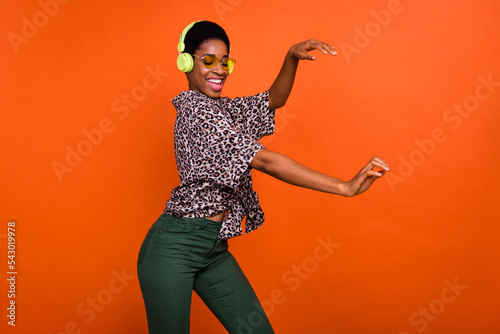 Portrait of attractive dreamy cheerful trendy funky girl listening hit melody dancing isolated over shine orange color background