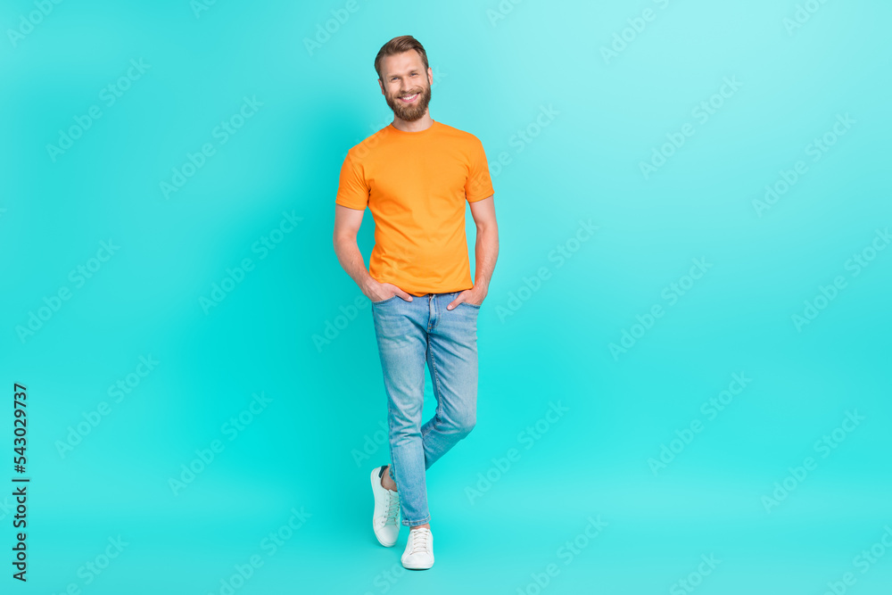 Full size photo of good mood handsome man with masculine beard dressed orange t-shirt arms in pockets isolated on teal color background Full size photo of good mood handsome man with masculine beard dressed orange t-shirt arms in pockets isolated on teal color background