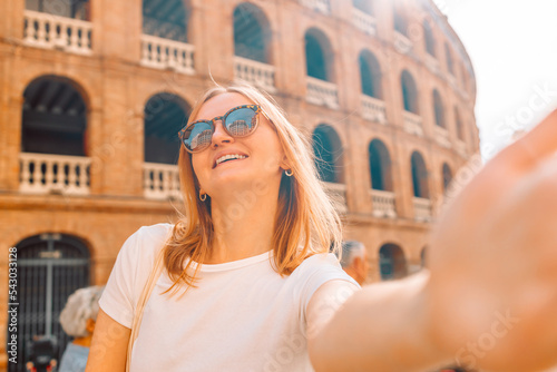 Young girl tourist in sunglasses making selfie photo on her smartphone in front of the famous Plaza de Toros de Valencia. Travel in Barcelona concept.  photo