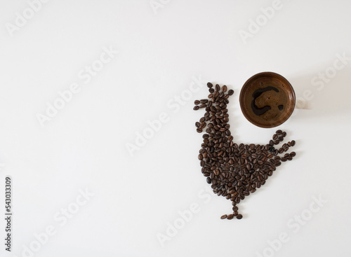 Creative concept of coffee beans and cup of coffee. Silhouette of rooster. Minimal natural pleasure. Thanksgiving design on white background. Flat lay with copy space.