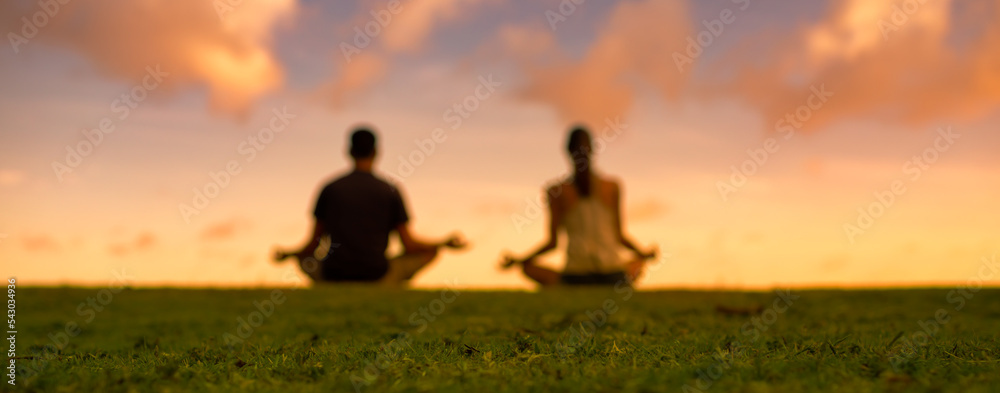 Obraz premium Blurred background of man woman meditating on grass facing sunset. 