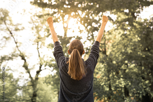 Young healthy active woman outdoors in nature feeling inspired with arms up 