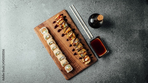 Top view of a set of delicious fresh sushi rolls, chopsticks, and soy sauce on a  wooden board