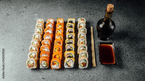 Set of delicious fresh sushi rolls, chopsticks, and soy sauce on a  gray surface