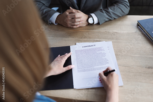 Cropped view of candidate signing contract near businessman during job interview.