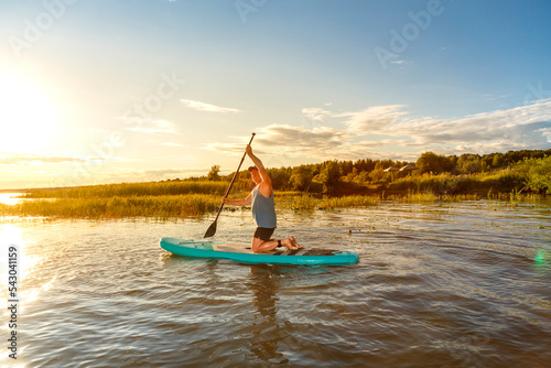 A man in shorts on a SUP board with a paddle floats on the water in the rays of the setting sun. photo