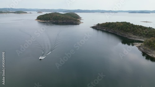 Aerial view of the water surface of Broken Bow Lake with a boat floating on the river, Oklahoma, USA. Autumn landscape of the coastline with a forest on the shore.